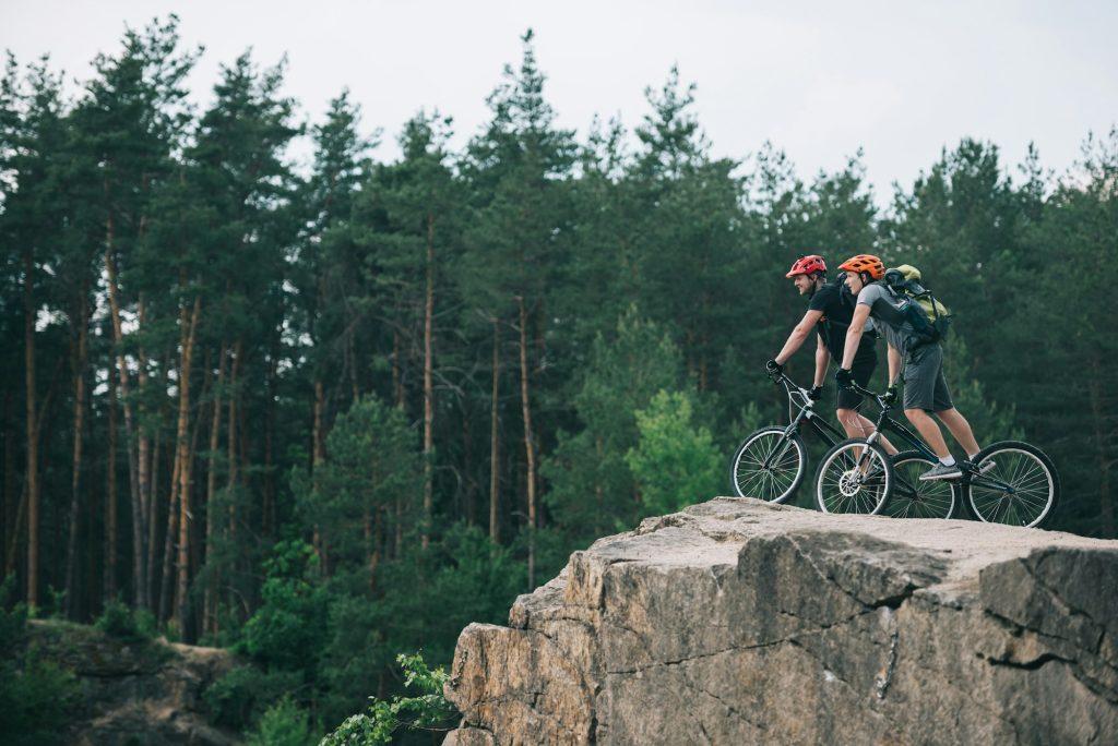 distant view of male extreme cyclists in protective helmets riding on mountain bicycles on rocky