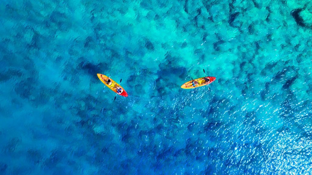 Kayaking. Aerial view of floating kayaks and people on blue sea at sunny day.